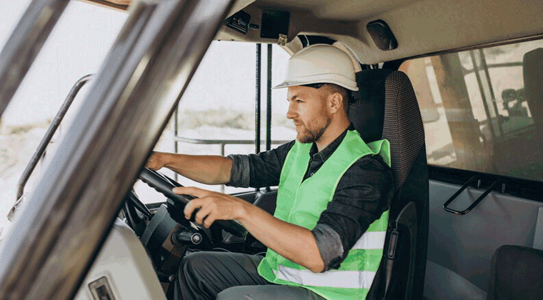 Homem uniformizado e de capacete de segurança dirigindo um caminhão