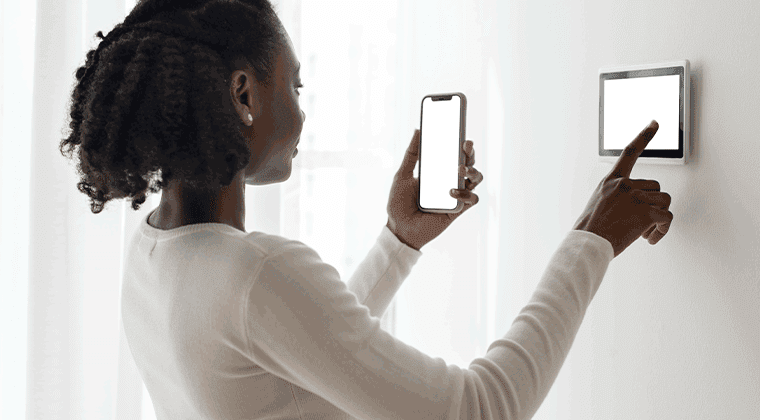 Uma mulher segurando um smartphone perto de um alarme na parede